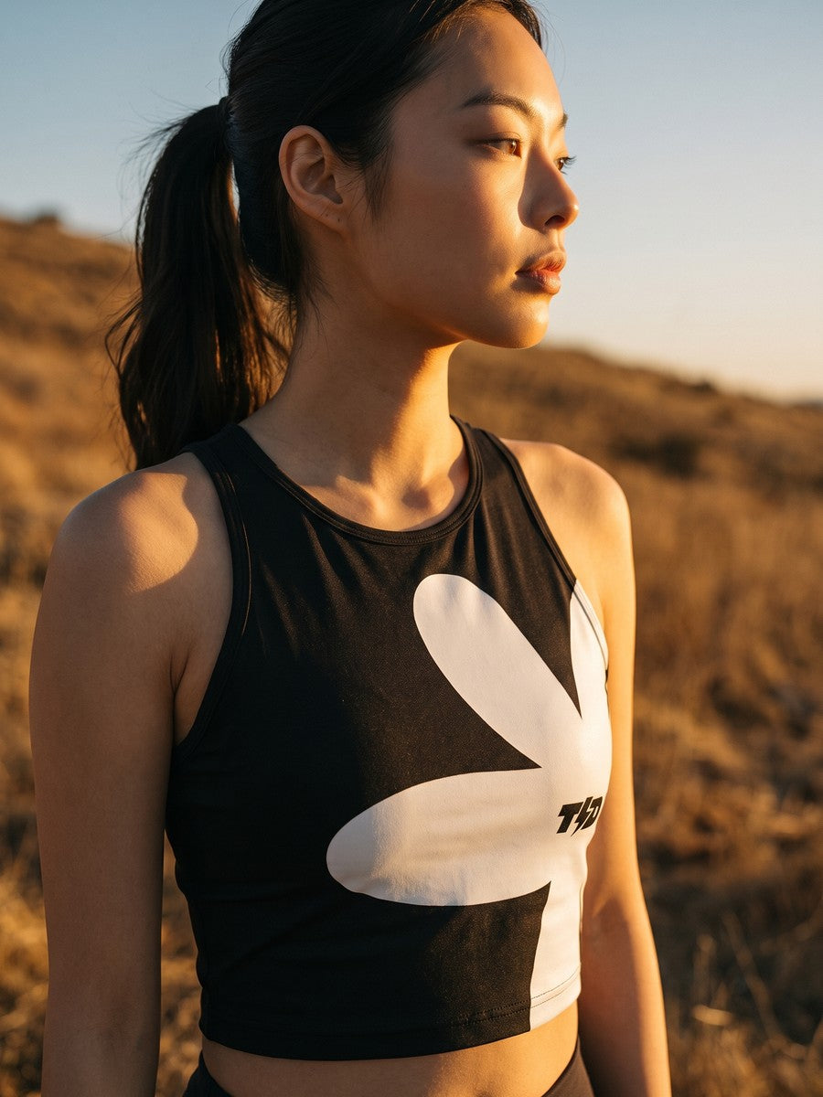 Woman in a black cropped tank top with a bold graphic print, backlit on a golden-hour hillside.