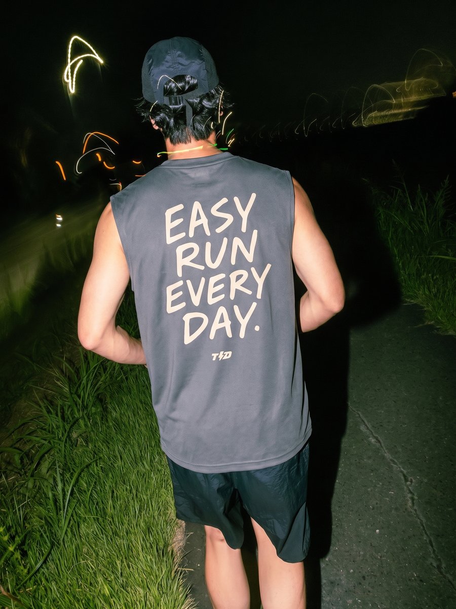 Man seen from behind on a night run, glowstick light trails streaking past, bold back-print graphic on his tee.